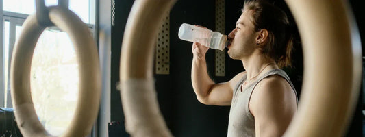 Man drinking from a water bottle at the gym after a workout, representing hydration and joint support with Supple joint health supplements.